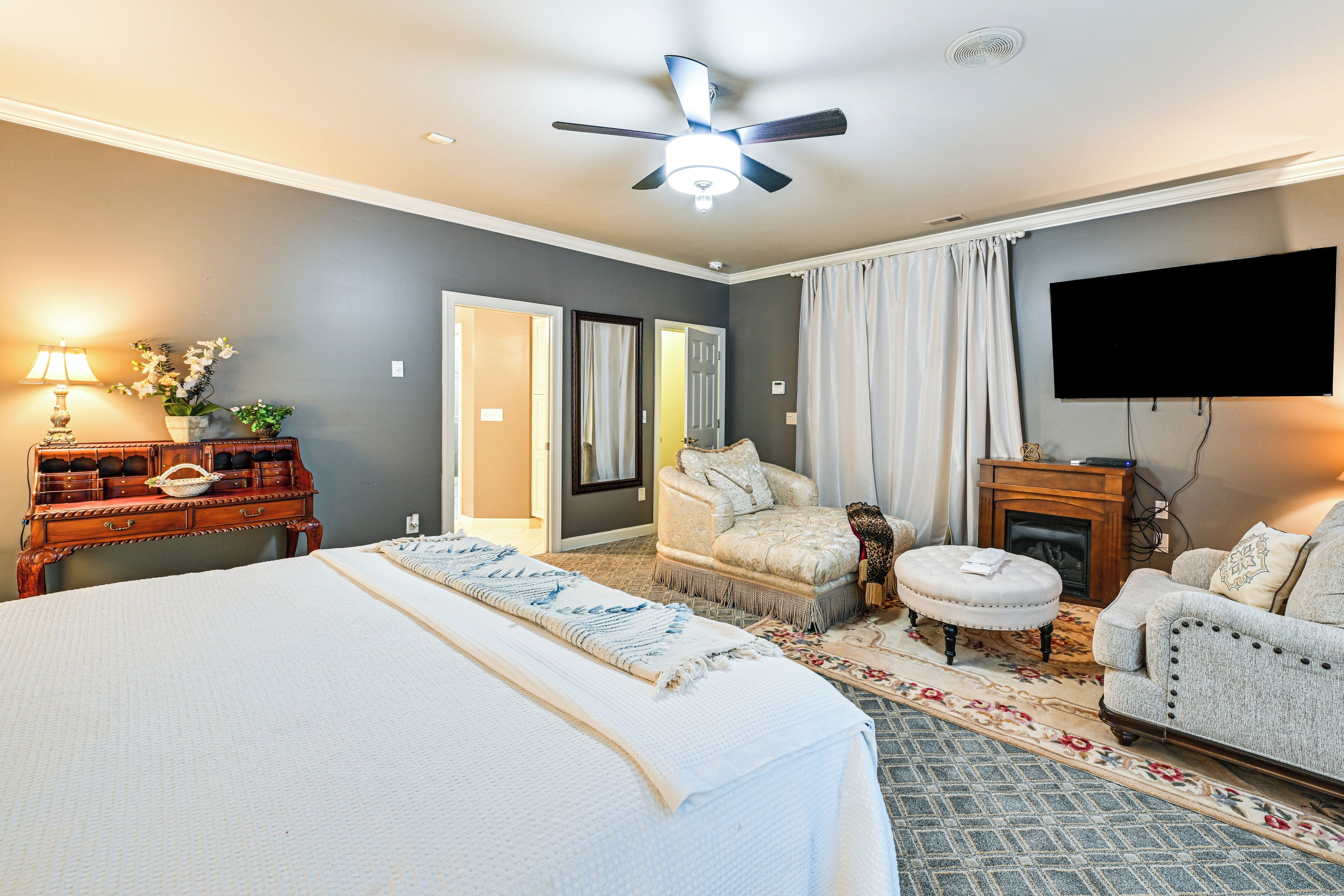A bedroom with a bed, a desk, a chair, a television, and a fireplace.