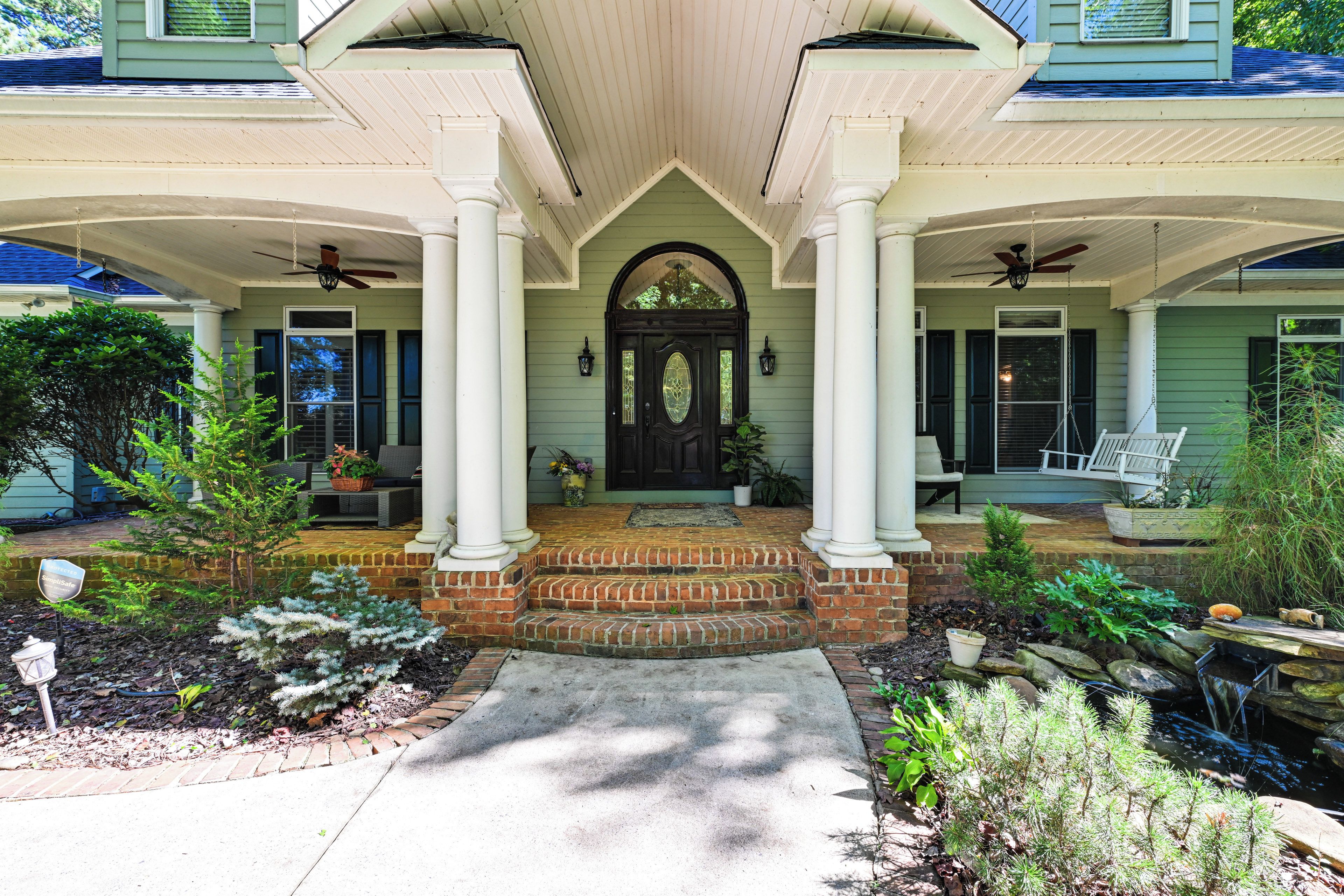A house with a front porch, two columns, a black door, and a small garden.