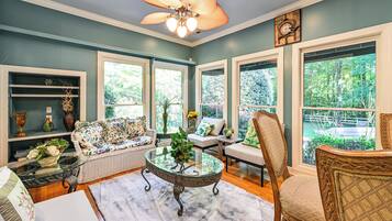 A spacious room with a ceiling fan, large windows, a sofa, a chair, and a table with a vase.