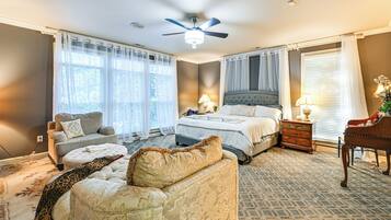 A bedroom with a bed, two bedside tables, a nightstand, a chair, a sofa, a ceiling fan, and a window with curtains.