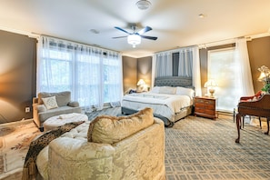 A bedroom with a bed, two bedside tables, a nightstand, a chair, a sofa, a ceiling fan, and a window with curtains.