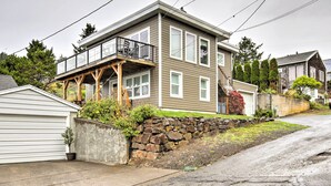 A two-story house with a balcony, a stone retaining wall, and a driveway. - Exquisite Oceanside House w/ Pacific Views & Deck! (Tillamook)