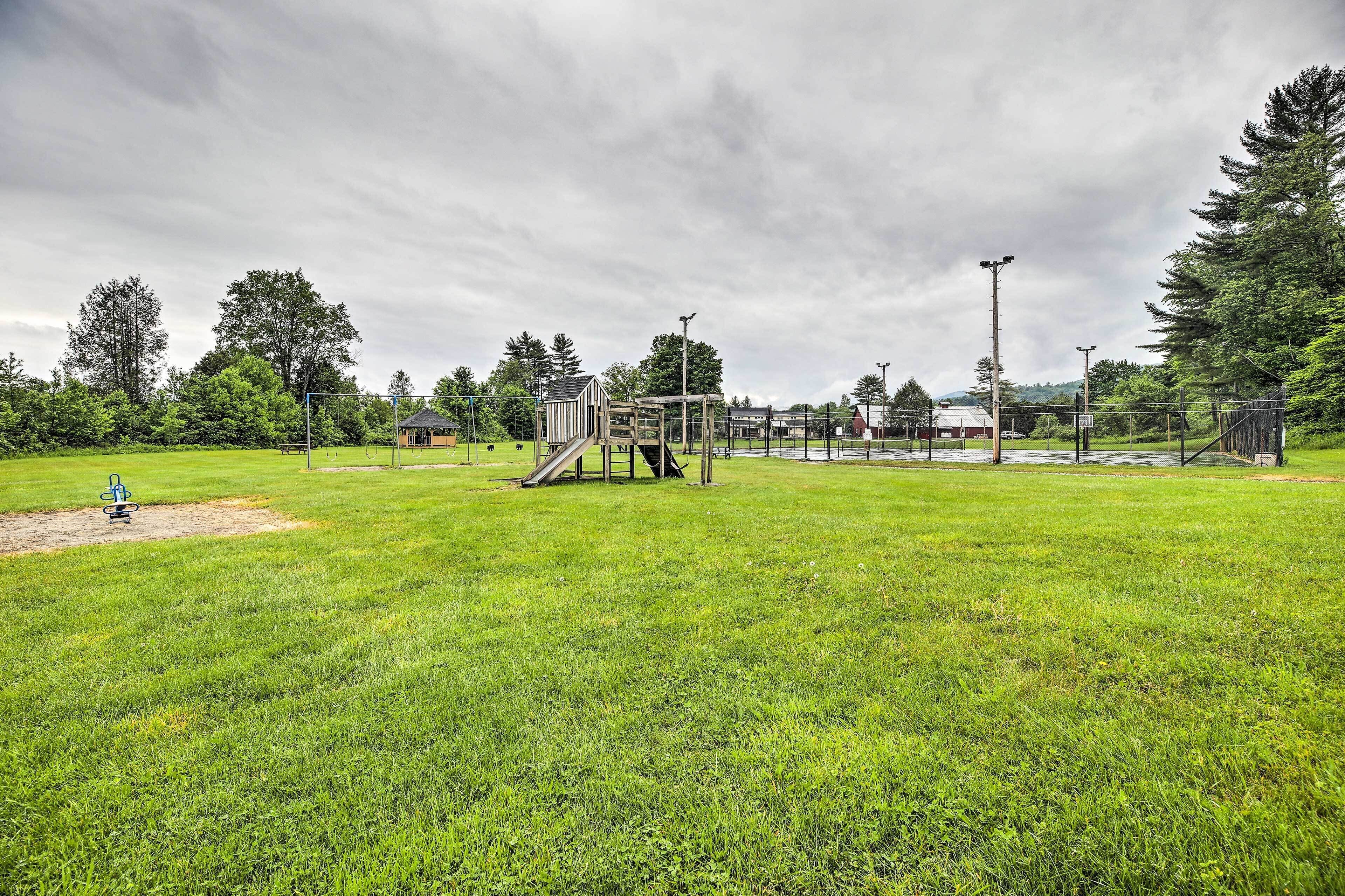 A park with a playground, a small building, and a fenced area.