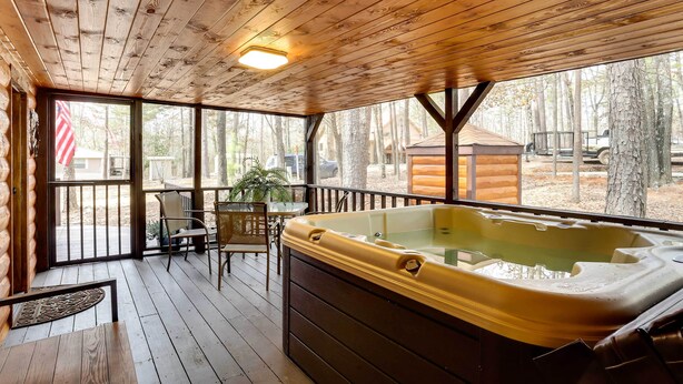 A wooden deck with a hot tub, outdoor seating, and a view of the surrounding forest. - Broken Bow Abode w/ Hot Tub < 7 Mi to Lake! (Broken Bow)