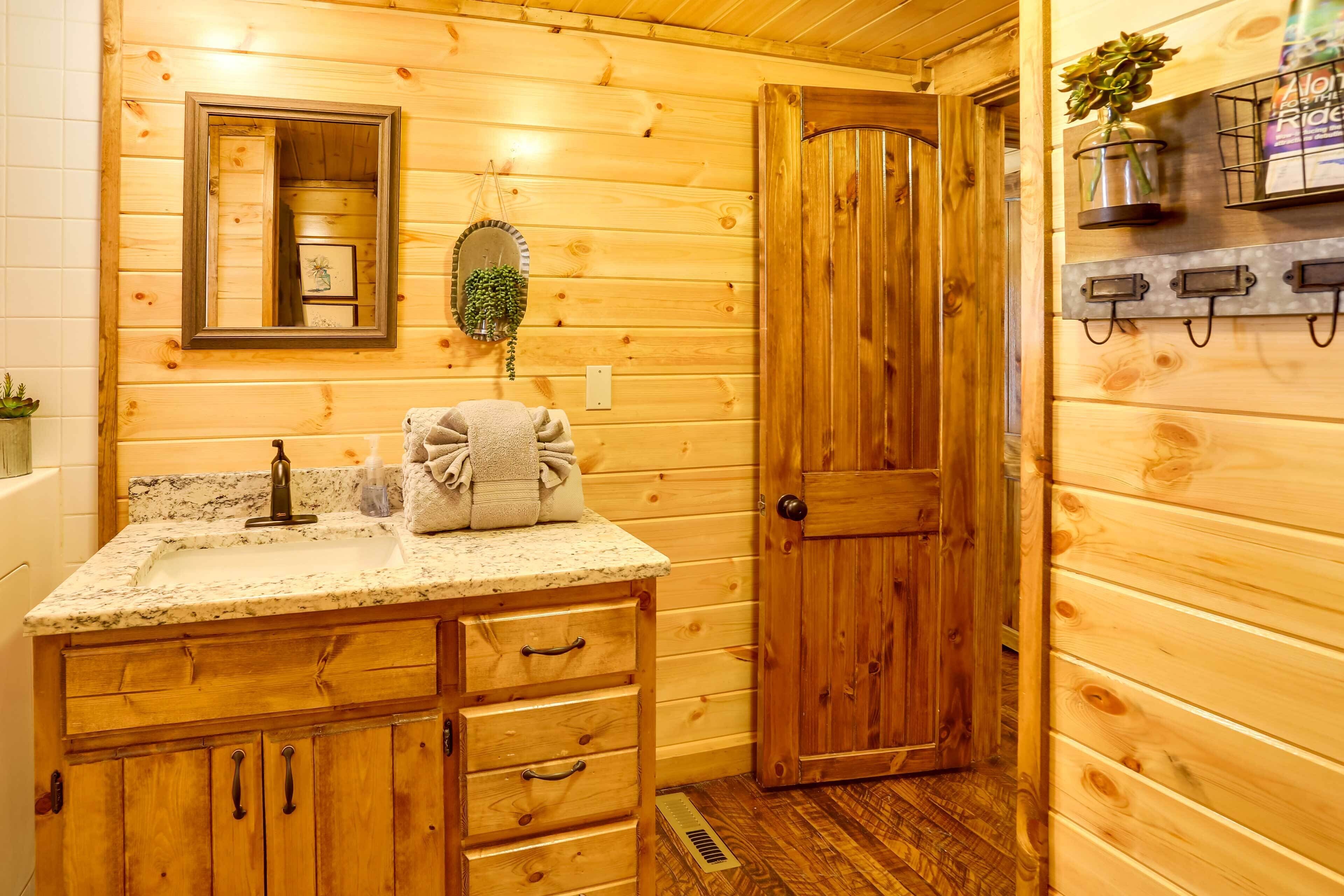 A wooden cabin bathroom with a granite countertop sink, wooden cabinets, a mirror, a towel rack, and a door.