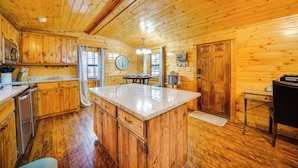 A wooden cabin interior with a kitchen, dining area, and a large wooden door. - Broken Bow Abode w/ Hot Tub < 7 Mi to Lake! (Broken Bow)