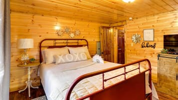 A wooden-paneled bedroom with a metal-framed bed, a bedside table with a lamp, and a decorative wall piece.