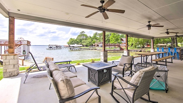 An outdoor patio with seating, tables, and ceiling fans overlooking a body of water. - Private Dock & Boat House: Lakefront Mabank Home (Mabank)