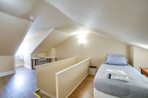 Un dormitorio con techo inclinado, una cama con almohadas, un escritorio pequeño con una silla y una ventana.