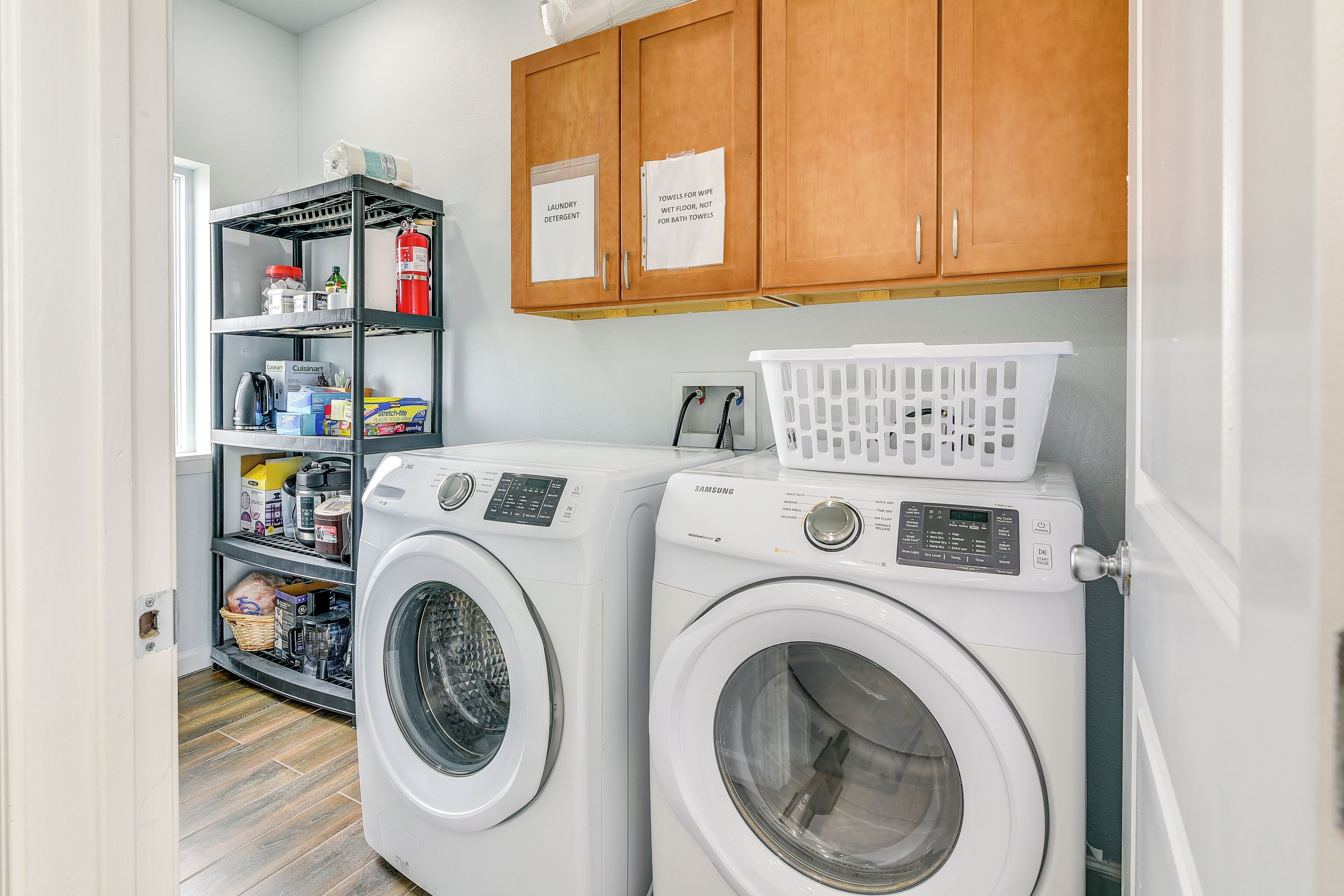 A laundry area with two front-loading washing machines, a shelf with laundry supplies, and wooden cabinets above.