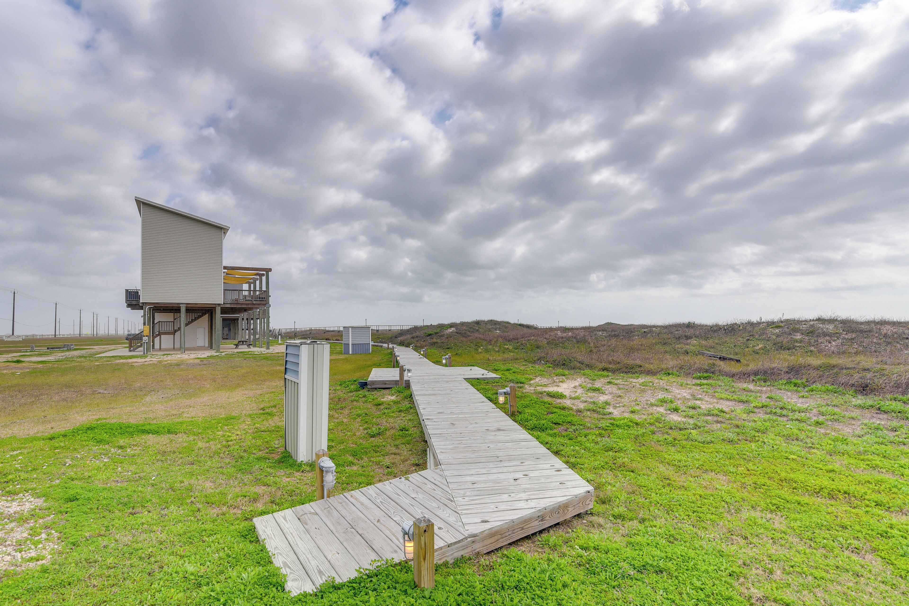 A wooden boardwalk leading to a building with a flat roof and a ramp.