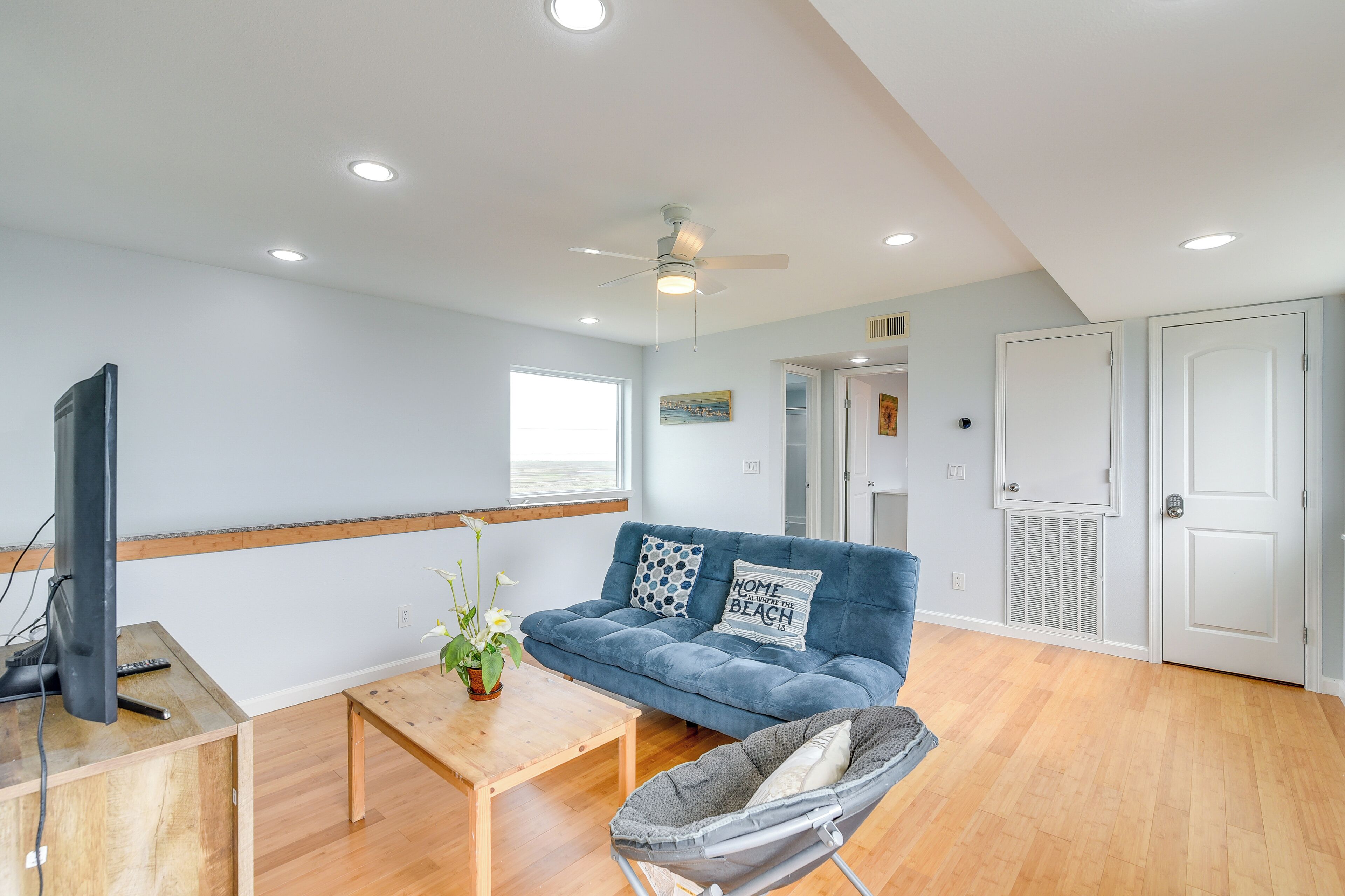 Un salon avec un canapé bleu, une table basse en bois, un téléviseur et un ventilateur de plafond.