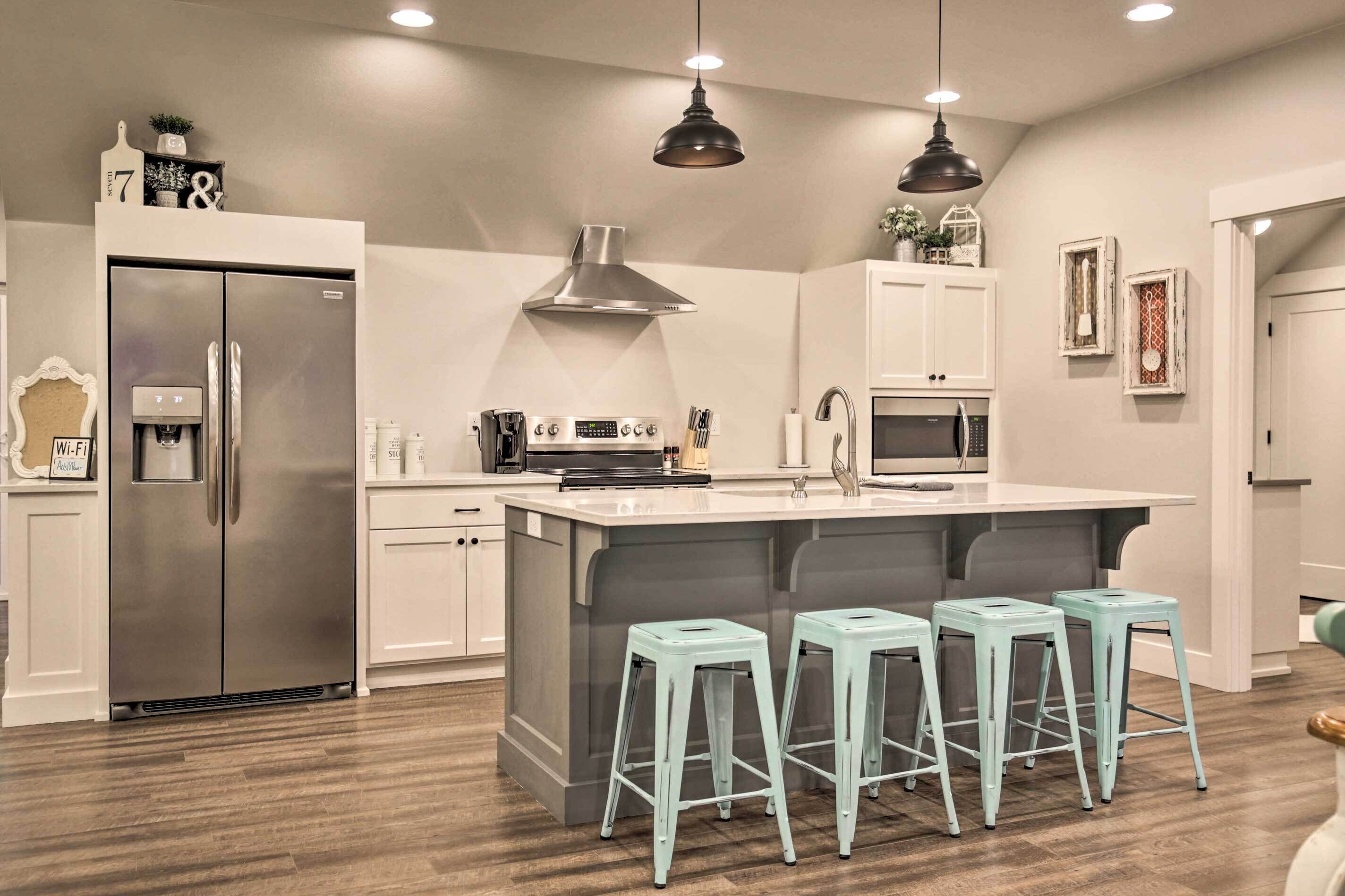 A modern kitchen with a stainless steel refrigerator, a built-in oven, a microwave, and a large island with bar stools.