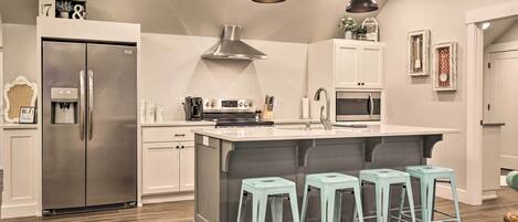 A modern kitchen with a stainless steel refrigerator, a built-in oven, a microwave, and a large island with bar stools.