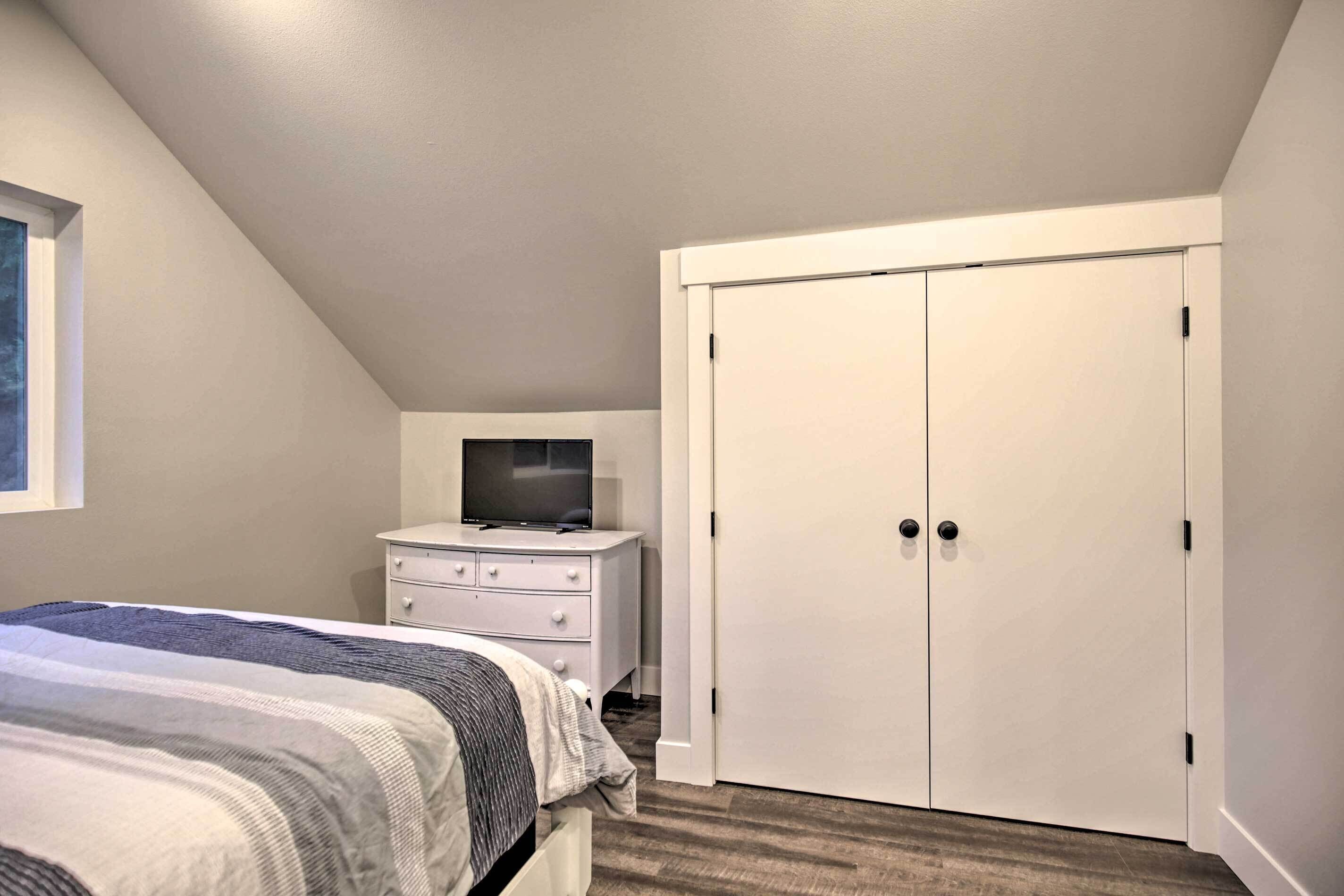 Une chambre à coucher avec un lit, une commode, un téléviseur et un placard.