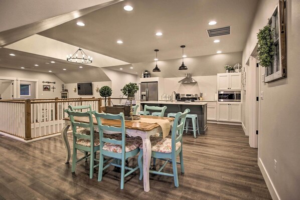 A spacious kitchen with modern appliances, a dining area with teal chairs, and a high ceiling with recessed lighting.