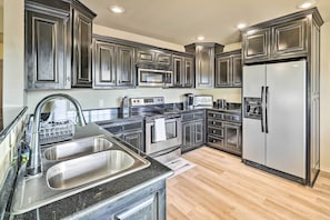 A modern kitchen with stainless steel appliances, dark cabinetry, and a black countertop. - Elegant Vacation Rental w/ Private Yard! (Springdale)