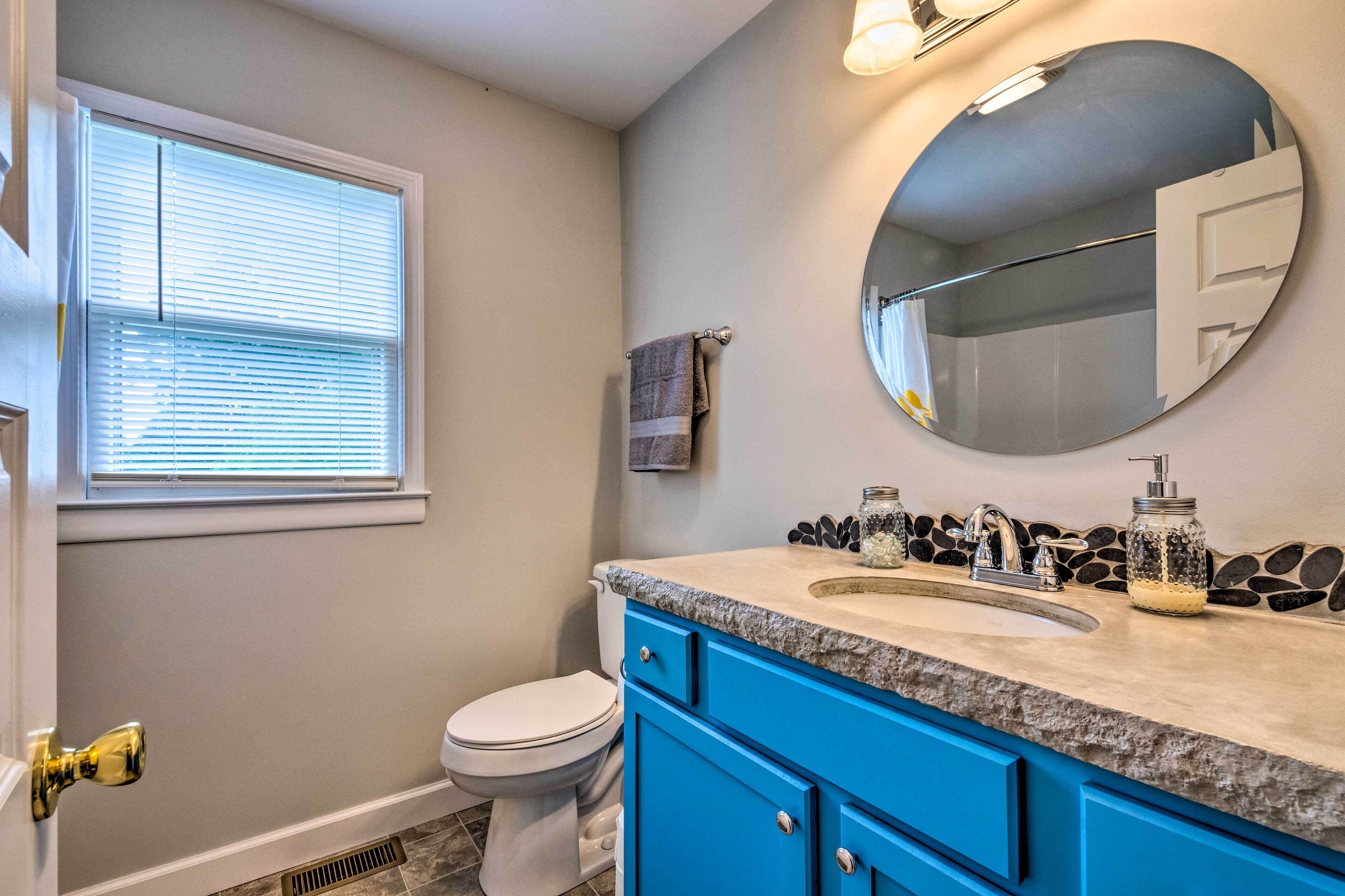 A bathroom with a toilet, sink, blue cabinets, a mirror, and a window with blinds.