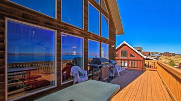 A wooden deck with a barbecue grill, outdoor seating, and large windows overlooking a scenic landscape.