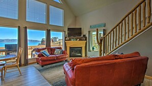 A spacious living room with a fireplace, leather sofas, and large windows overlooking a scenic view. - Garden City Lake House: Hot Tub & Views! (Garden City)