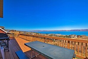Eine Holzterrasse mit Tisch und Grill mit Blick auf einen See und entfernte Berge.