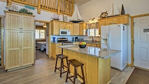 A spacious kitchen with wooden cabinets, a central island with stools, a refrigerator, and a microwave. - Garden City Lake House: Hot Tub & Views! (Garden City)