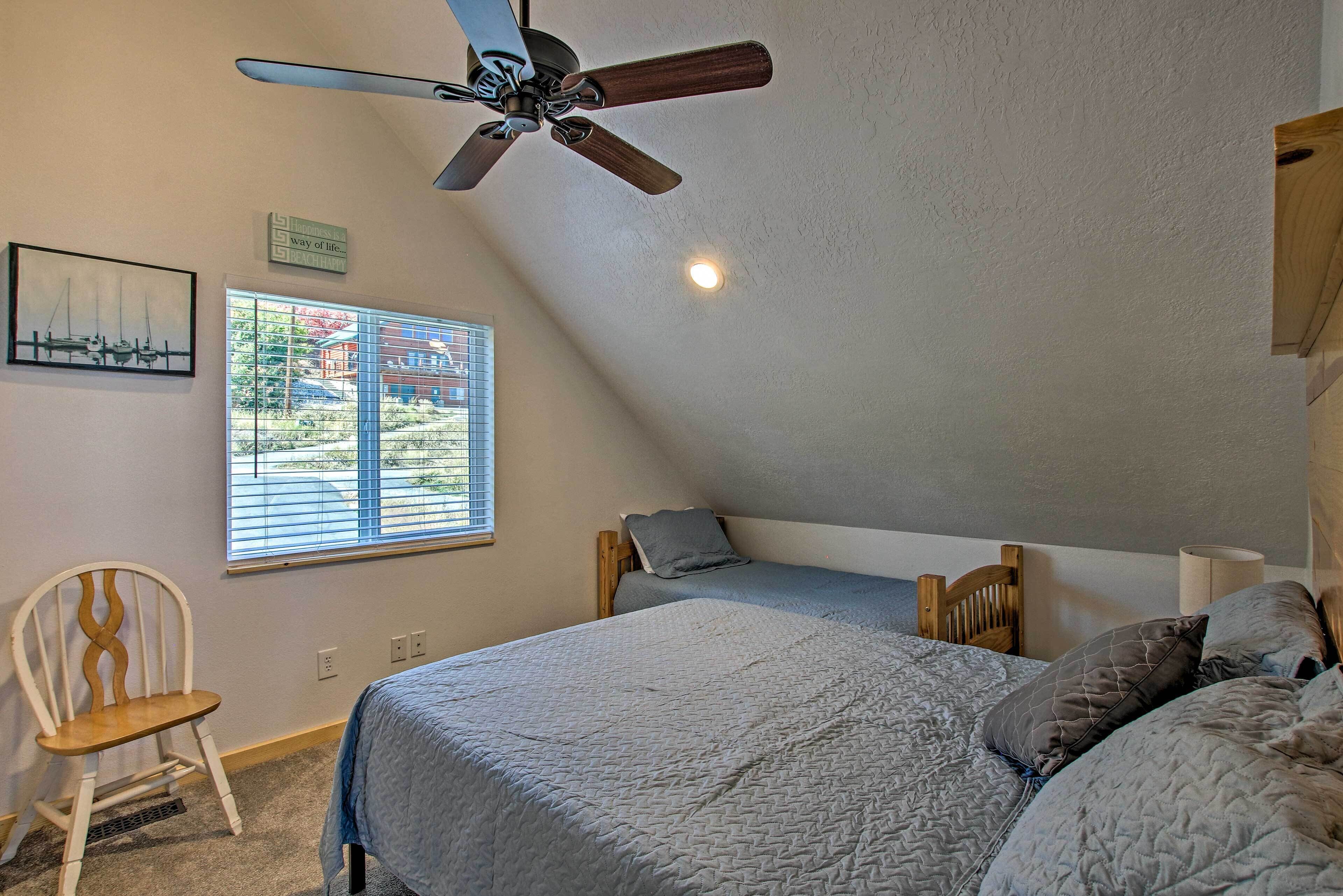 A bedroom with a bed, a ceiling fan, a window with blinds, a chair, and a wall-mounted light fixture.