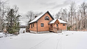 Una cabaña de troncos con techo inclinado, un porche delantero y un paisaje cubierto de nieve.