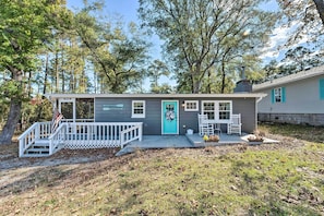 A small, single-story cabin with a front porch, a turquoise door, and a white railing.