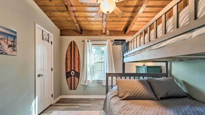 Une chambre avec un lit superposé, un plafond en bois, une décoration sur le thème du surf et une porte.