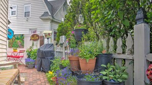 A garden with potted plants, a covered table, and a red chair. - Historic Ocean Grove Home - Walk to Beach! (Ocean Grove)