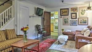 A living room with a sofa, a coffee table, a TV on a shelf, a dining area with a table and chairs, and a kitchen visible through an open door. - Historic Ocean Grove Home - Walk to Beach! (Ocean Grove)