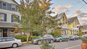 A street view with parked cars, a house with a porch, and a tree in the foreground. - Historic Ocean Grove Home - Walk to Beach! (Ocean Grove)
