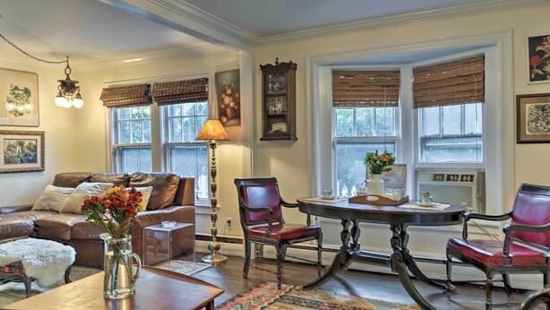 A cozy living room with a brown leather sofa, a wooden coffee table, and a patterned rug. There is a dining table with chairs and a chandelier hanging above. - Historic Ocean Grove Home - Walk to Beach! (Ocean Grove)