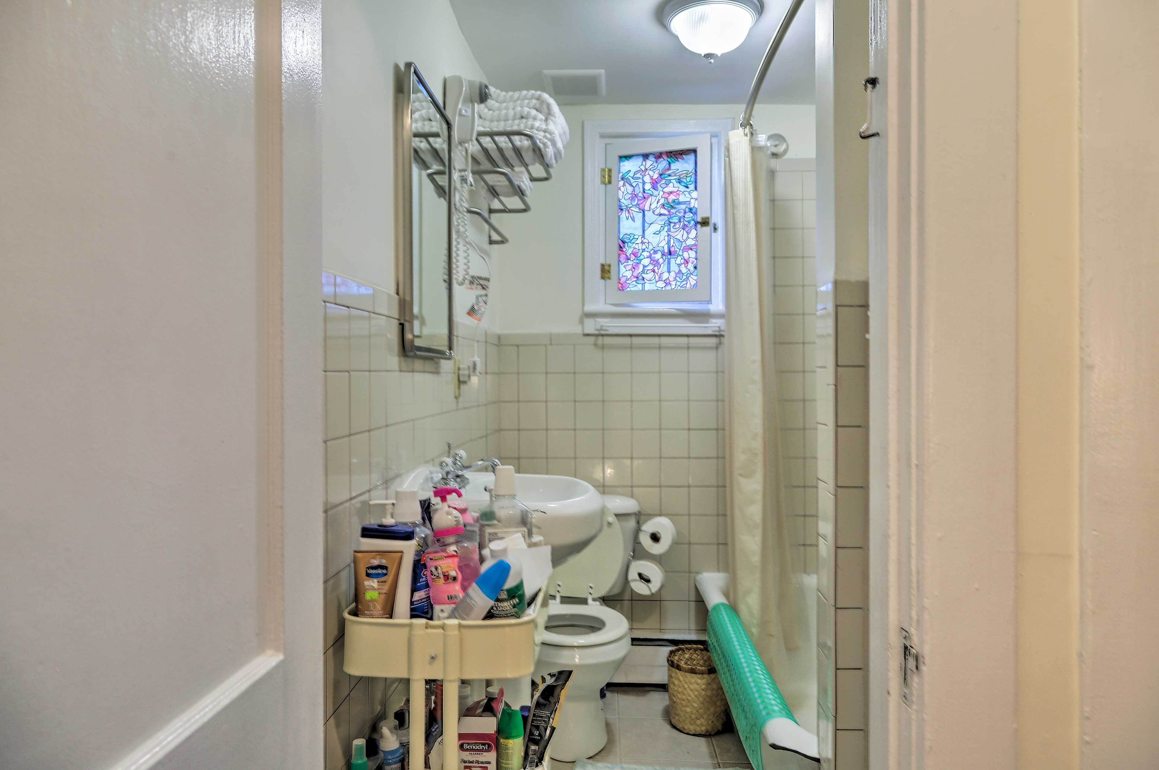 A bathroom with a toilet, sink, and shower. There is a window with a stained glass design.