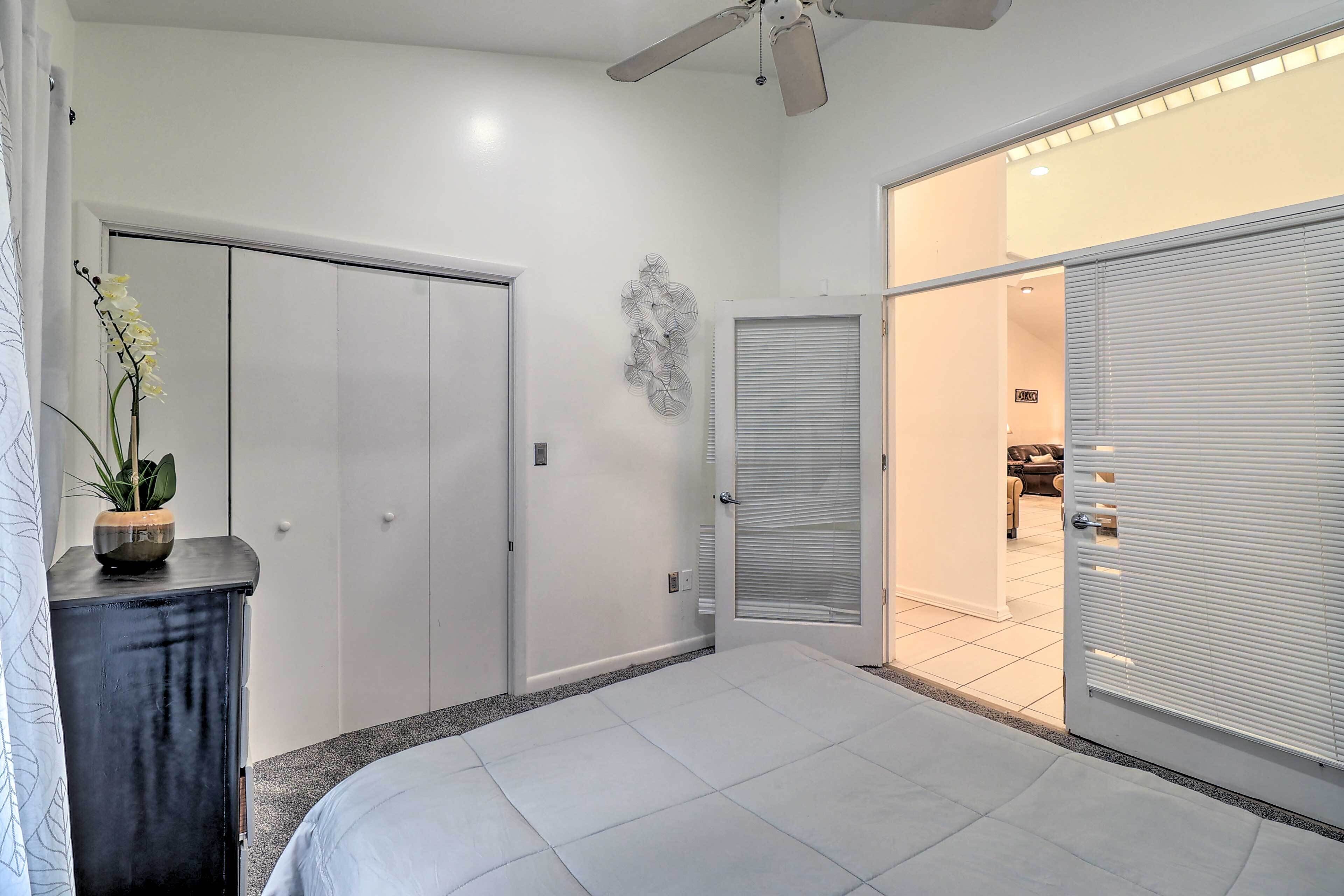A bedroom with a bed, a wardrobe, a ceiling fan, and a door leading to another room.
