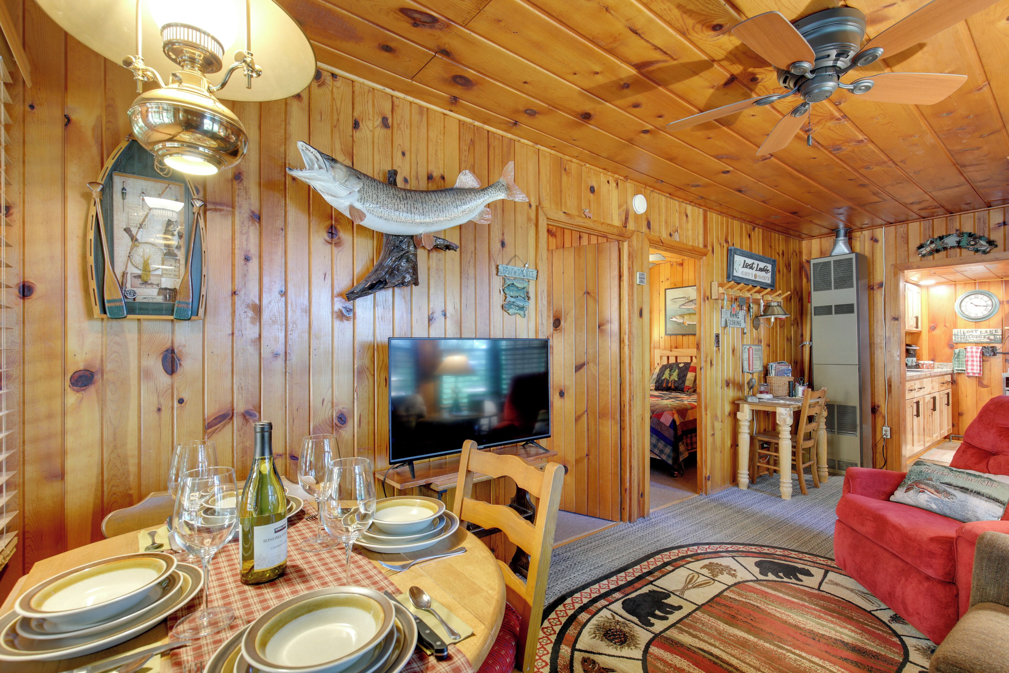 A wooden interior with a dining table set for four, a television, and a red sofa.