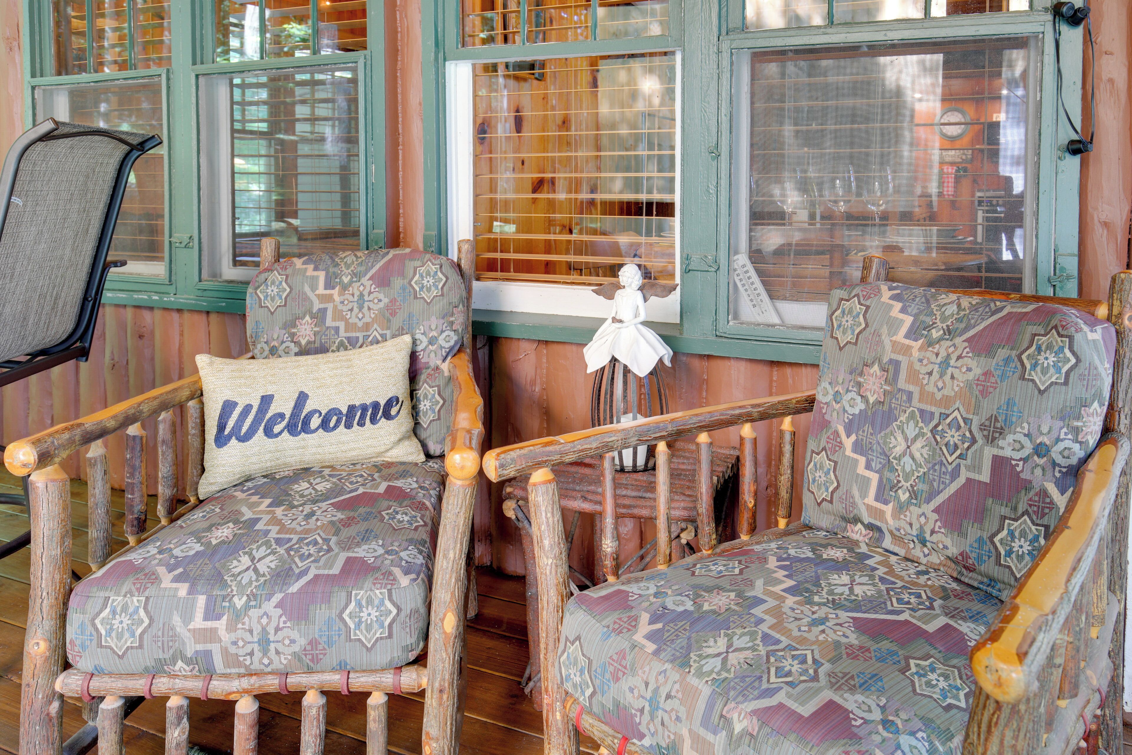 Two patterned armchairs with a 'Welcome' pillow, a wooden chair, and a window with blinds.