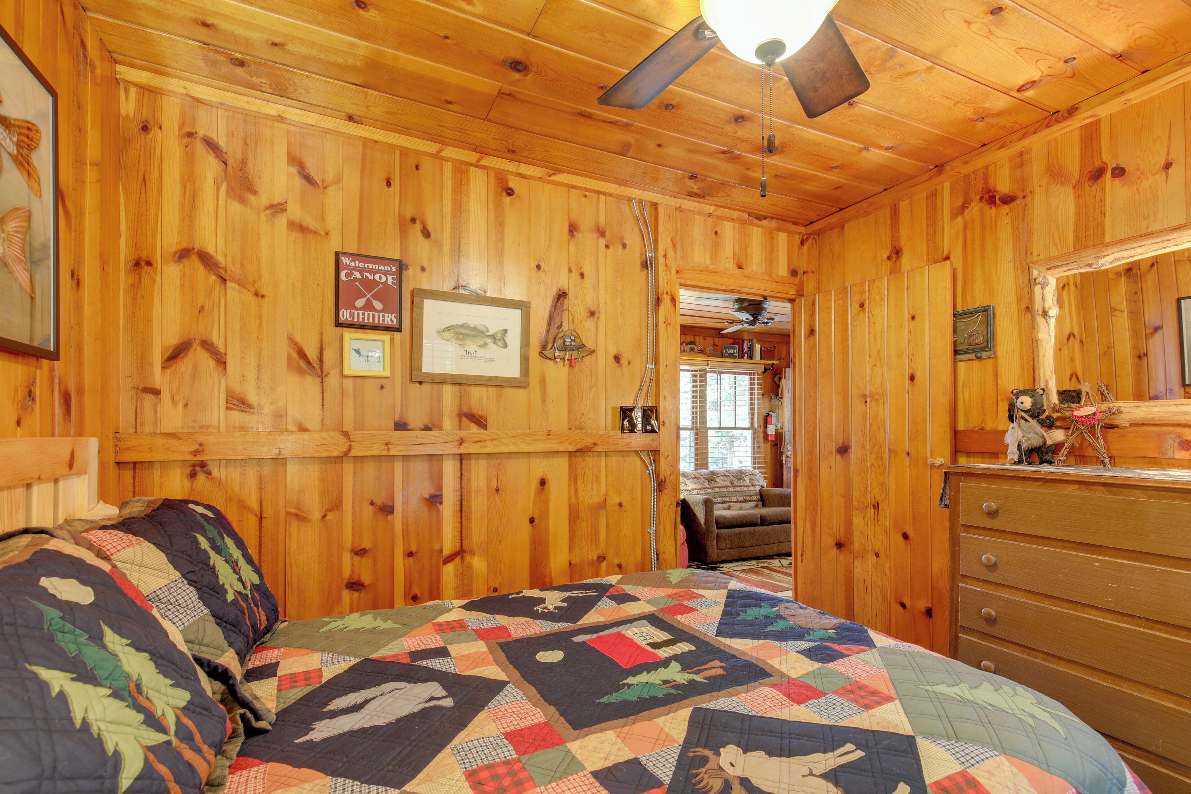 A wooden cabin bedroom with a bed, a dresser, and a ceiling fan.