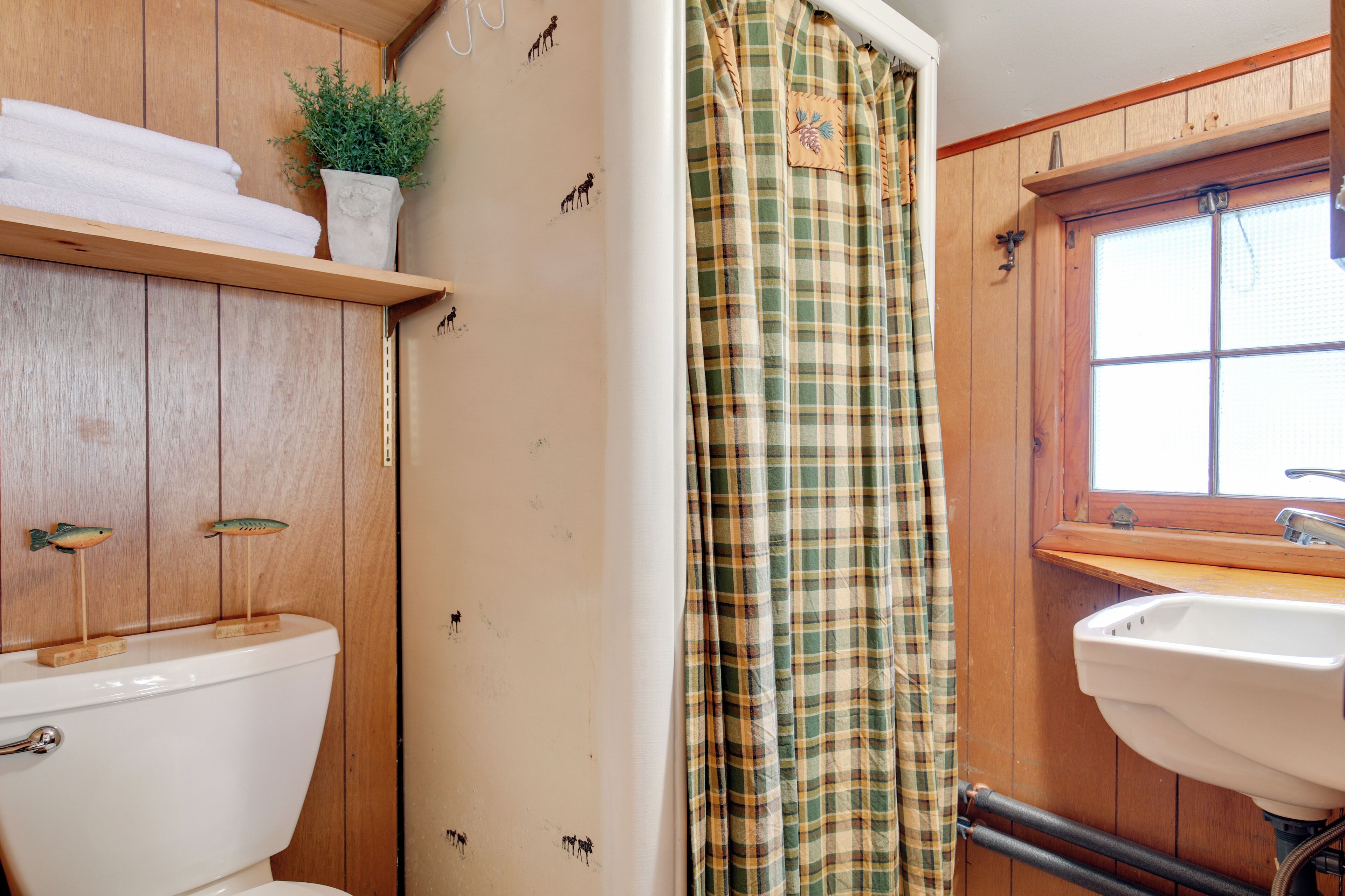 Une salle de bain avec des murs en bois, des toilettes, un lavabo et un rideau de douche.