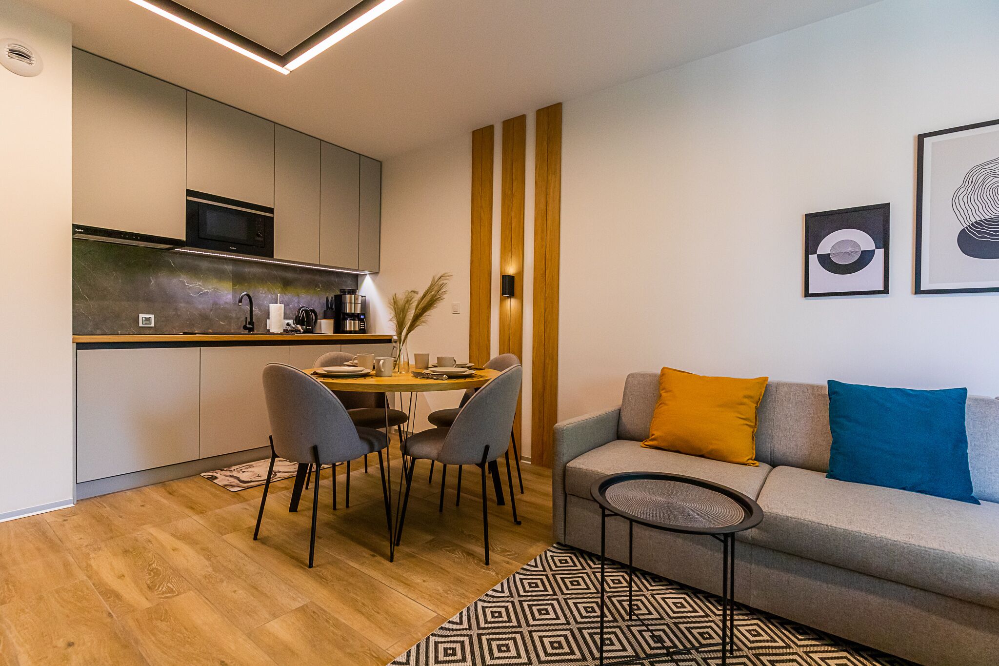 Eine moderne Küche mit Essbereich, einer Couch mit Kissen und Kunstwerken an der Wand.