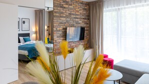 A modern hotel room with a brick accent wall, a flat-screen TV, a bed with blue bedding, a small round table, and a sofa. - RentPlanet - Stone Hill (Szklarska Poreba)