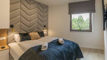 Une chambre moderne avec un grand lit, une tête de lit ornée d’un motif géométrique, une table de chevet avec une lampe et une fenêtre donnant sur des arbres.