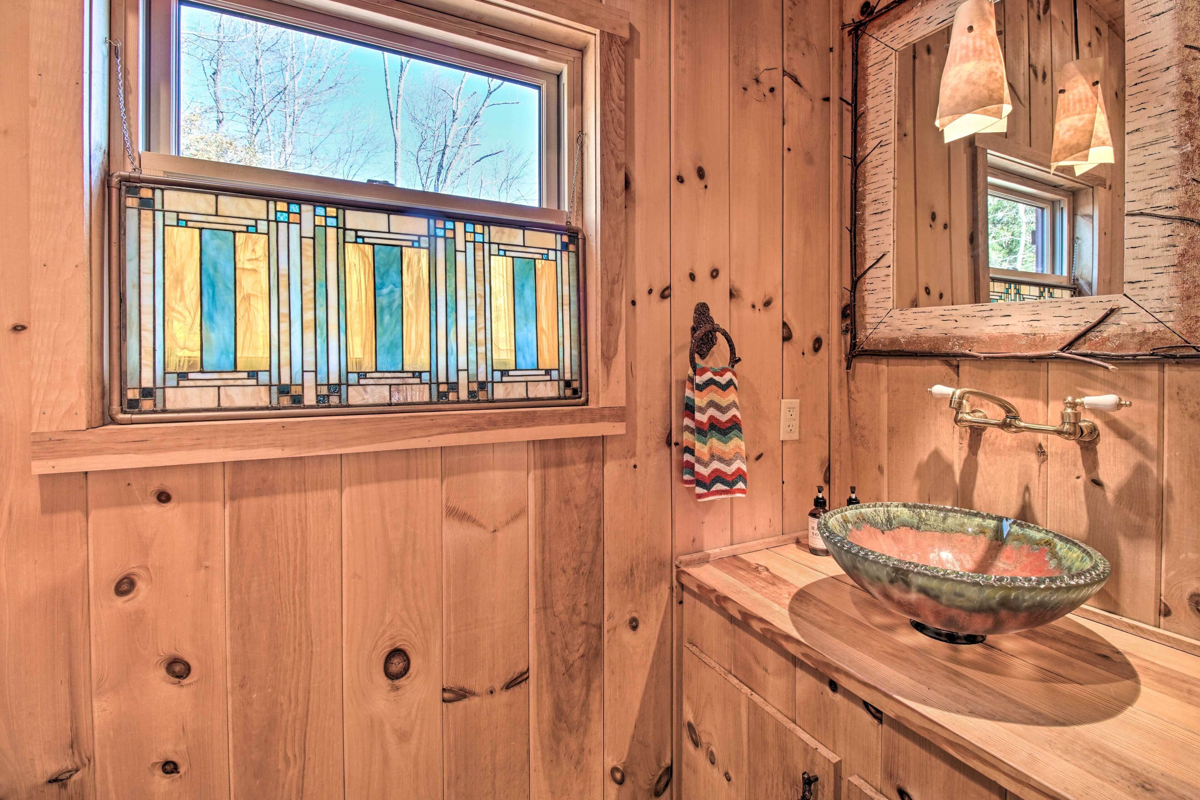 A wooden interior with a stained glass window, a wooden sink with a decorative bowl, and a mirror.