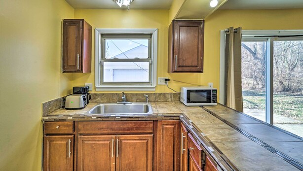 A kitchen with wooden cabinets, a sink, a window, and a microwave. - Inkster Home Near Airport & Henry Ford Museum (Inkster)