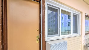 Un mur extérieur de couleur beige, avec une fenêtre et une grille d’aération.