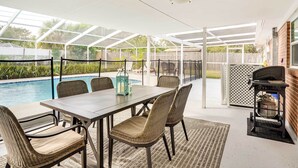 Een overdekt terras met een zwembad, buitenmeubels en een barbecue.