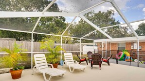 Een afgesloten patio met witte lounge fauteuils, potplanten en een bakstenen muur op de achtergrond.
