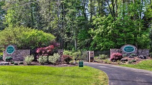 A landscaped entrance with a stone wall, two signs reading "Cades Cove Reserve," and a paved road leading into the property. - Townsend Condo w/ Pool, Great Smoky Mountain Views (Townsend)