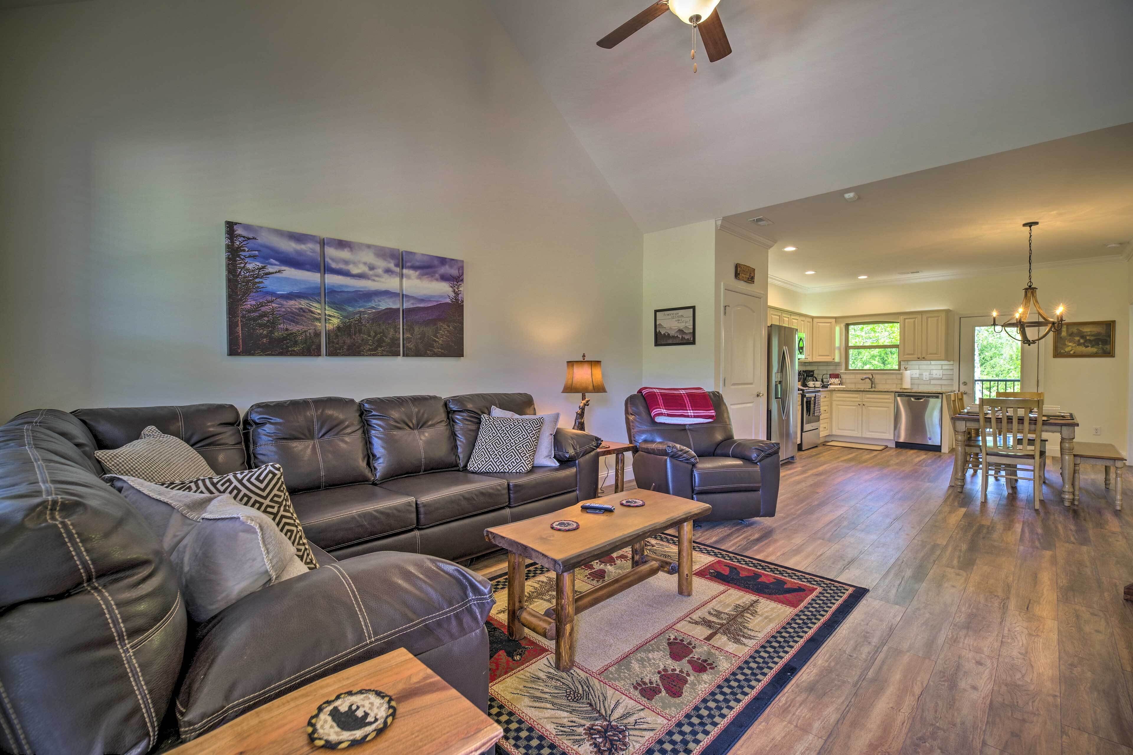 A spacious living room with a leather sofa, a wooden coffee table, and a patterned rug. A dining area with a wooden table and chairs is visible in the background.